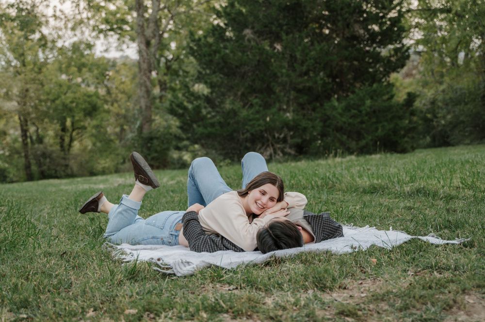 Girl gazes into fiancés eyes as they lay together on picnic blanket