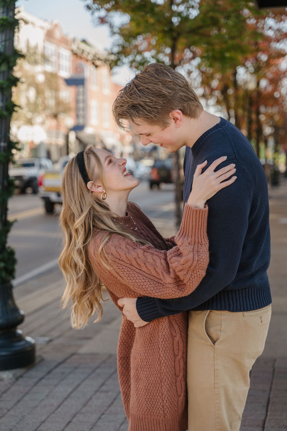 A couple laughs as they stand on the corner of a cozy, fall town