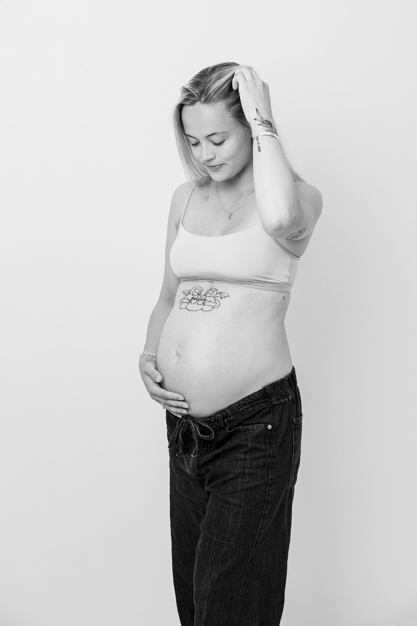 A black and white series showing a pregnant person's cropped torso wearing jeans and a white top against a light background.