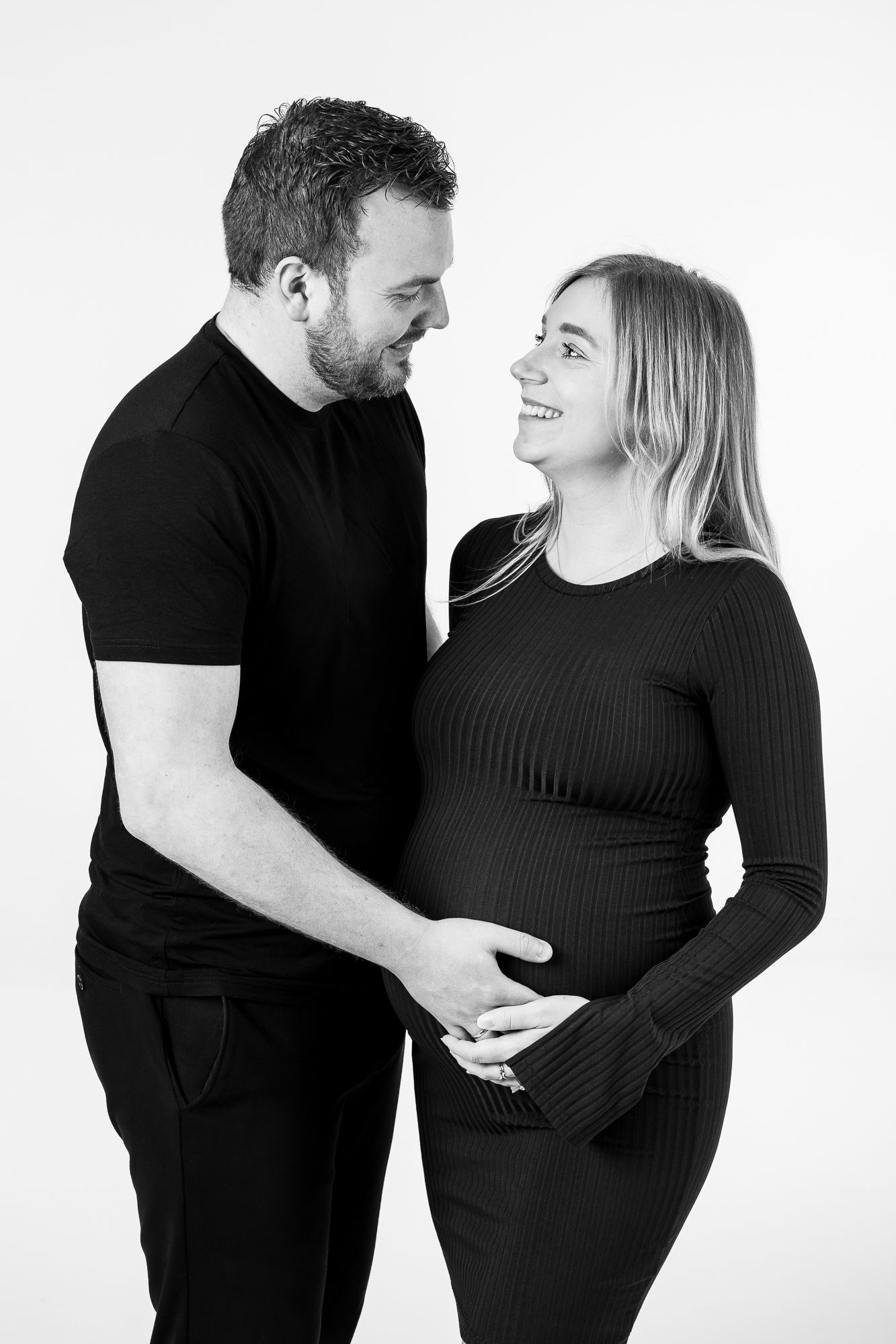 A loving black and white maternity photo shows a couple sharing an intimate moment as they cradle her pregnant belly.