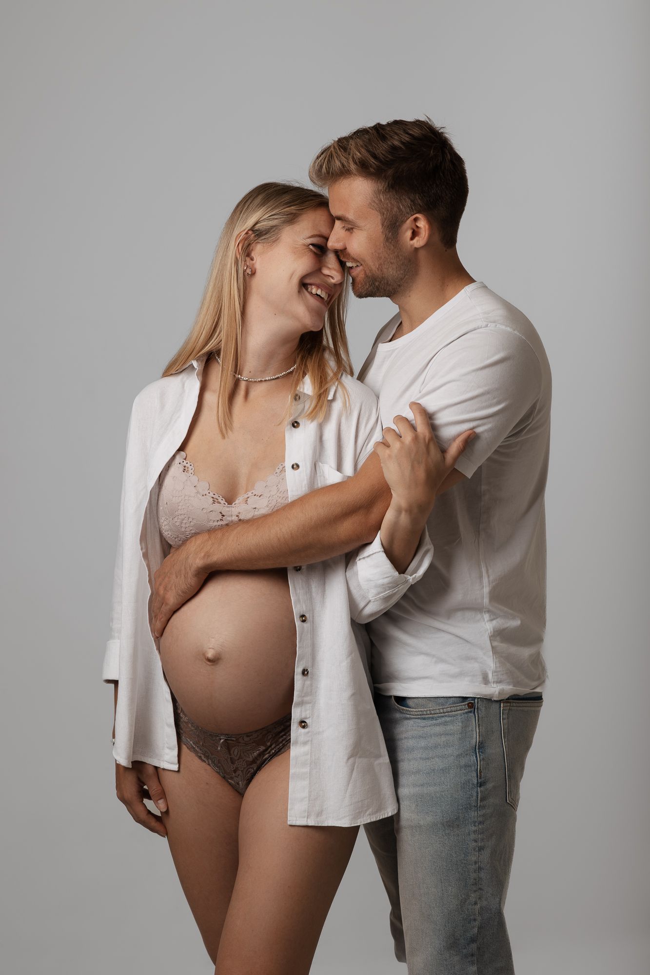 Intimate maternity photo series showing tender moments between an expecting couple against a plain backdrop.
