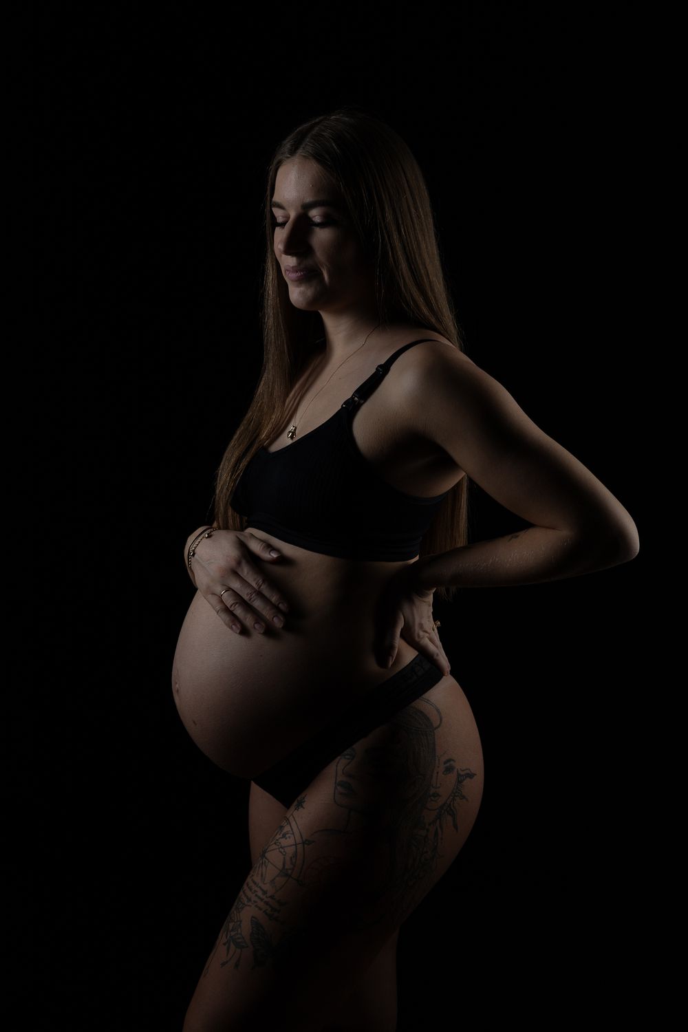 A low-key maternity silhouette photograph shows a pregnant figure in black against a dark background.