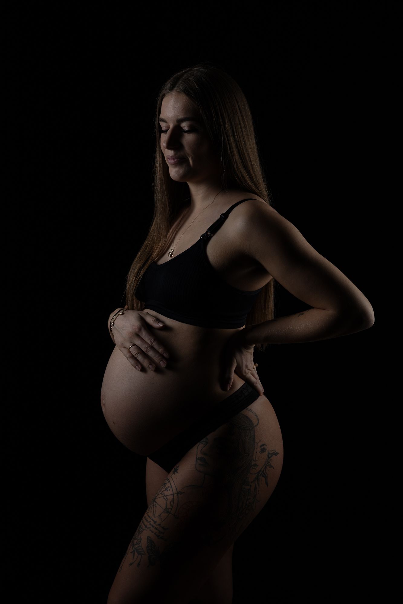 A low-key maternity silhouette photograph shows a pregnant figure in black against a dark background.