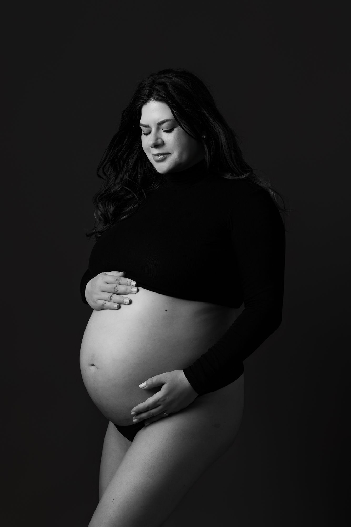 Artistic black and white maternity photo series showing a pregnant belly in four progressive stages against dark background.