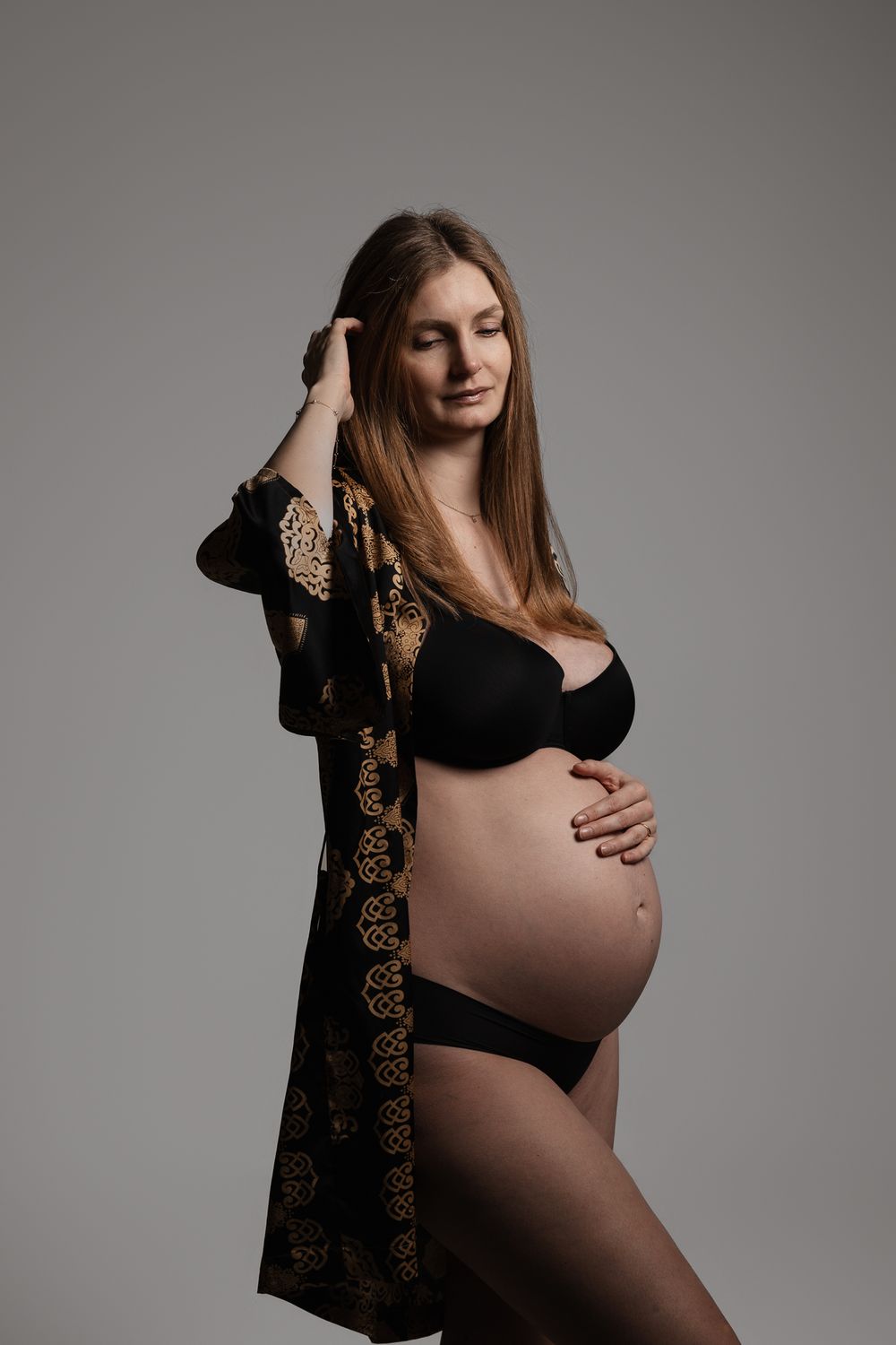 A maternity photo series showing a pregnant woman in black dress against grey backdrop with artistic lighting and poses.