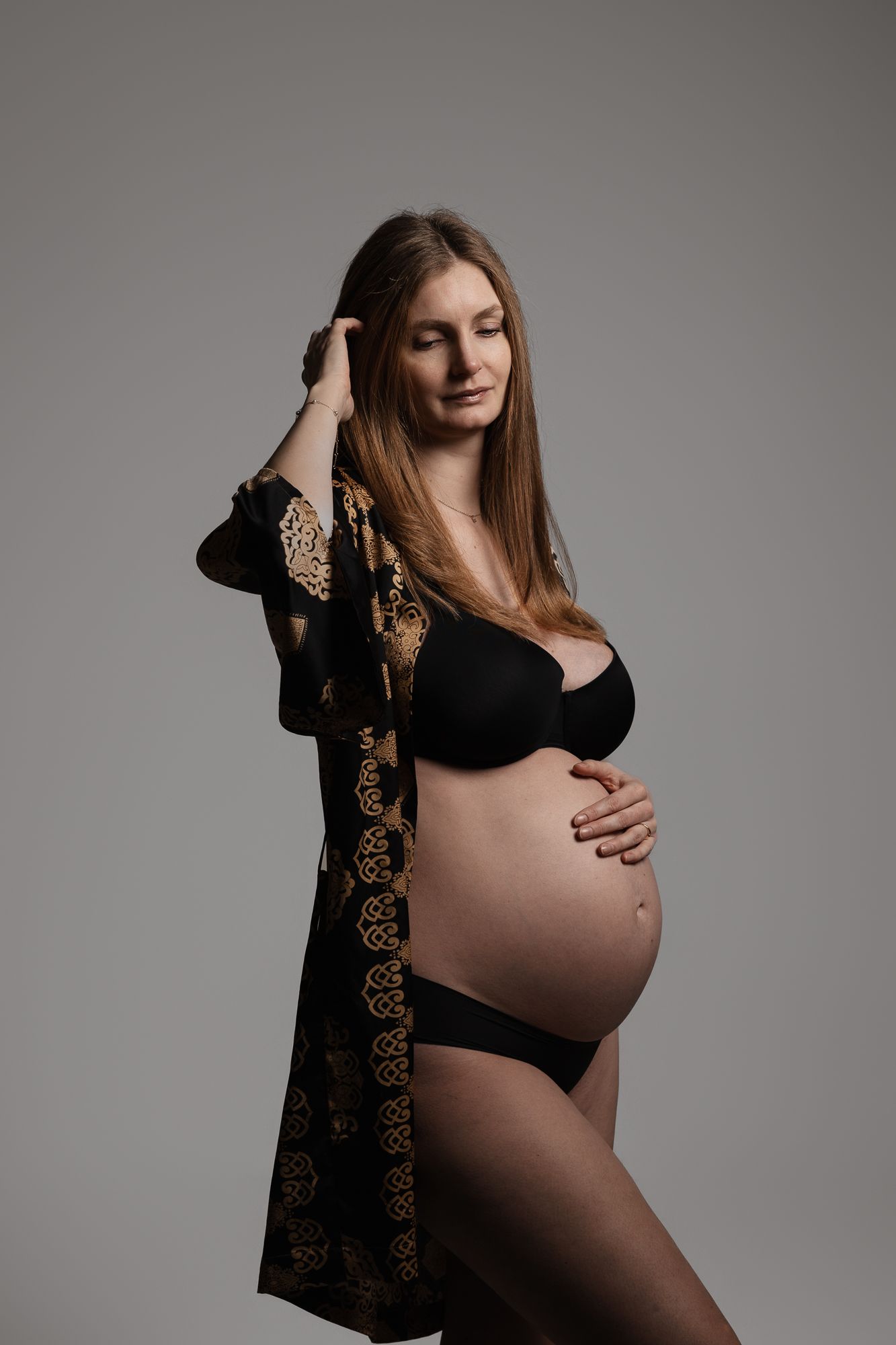 A maternity photo series showing a pregnant woman in black dress against grey backdrop with artistic lighting and poses.