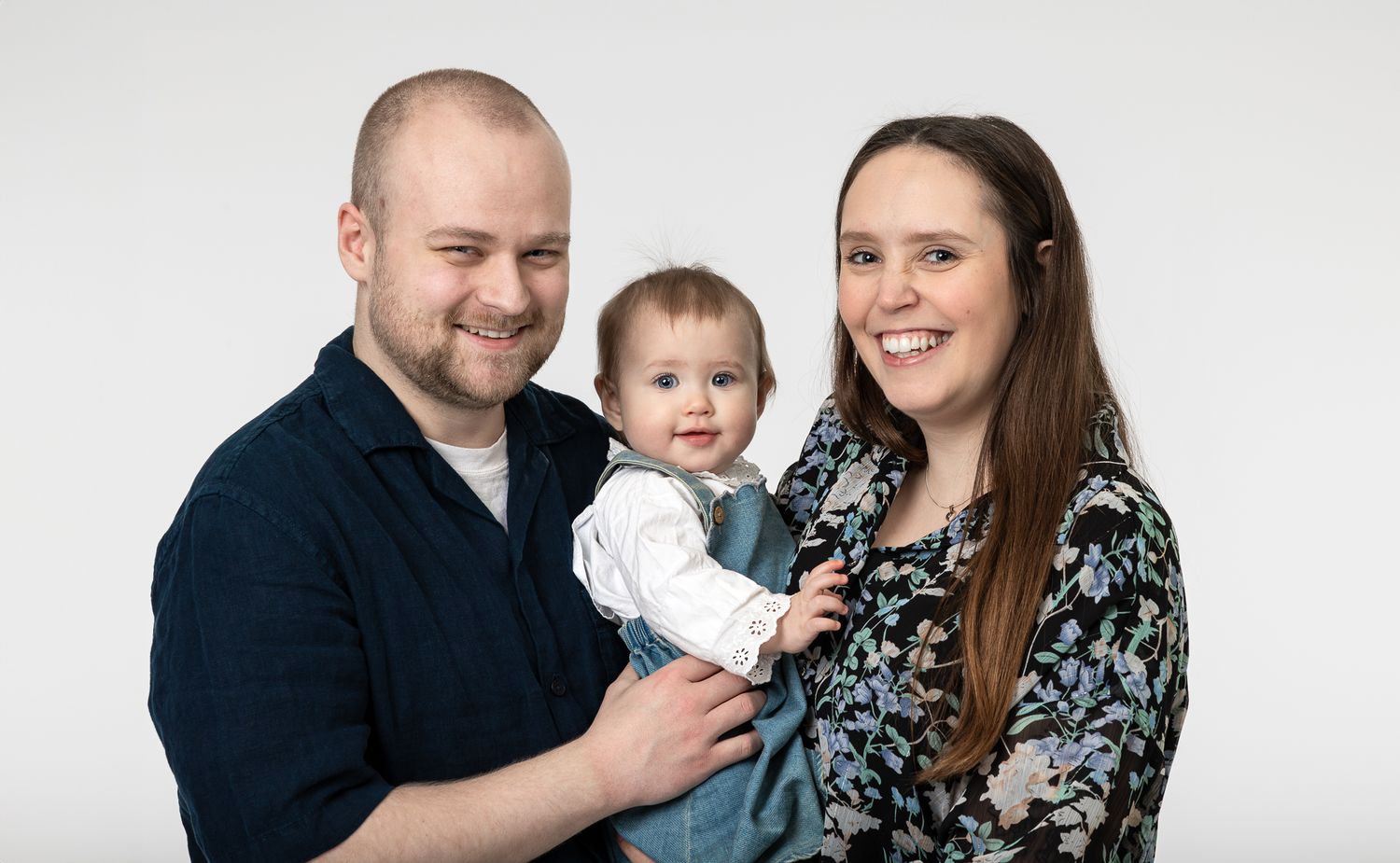 A family poses together against a light gray studio backdrop for a portrait session.