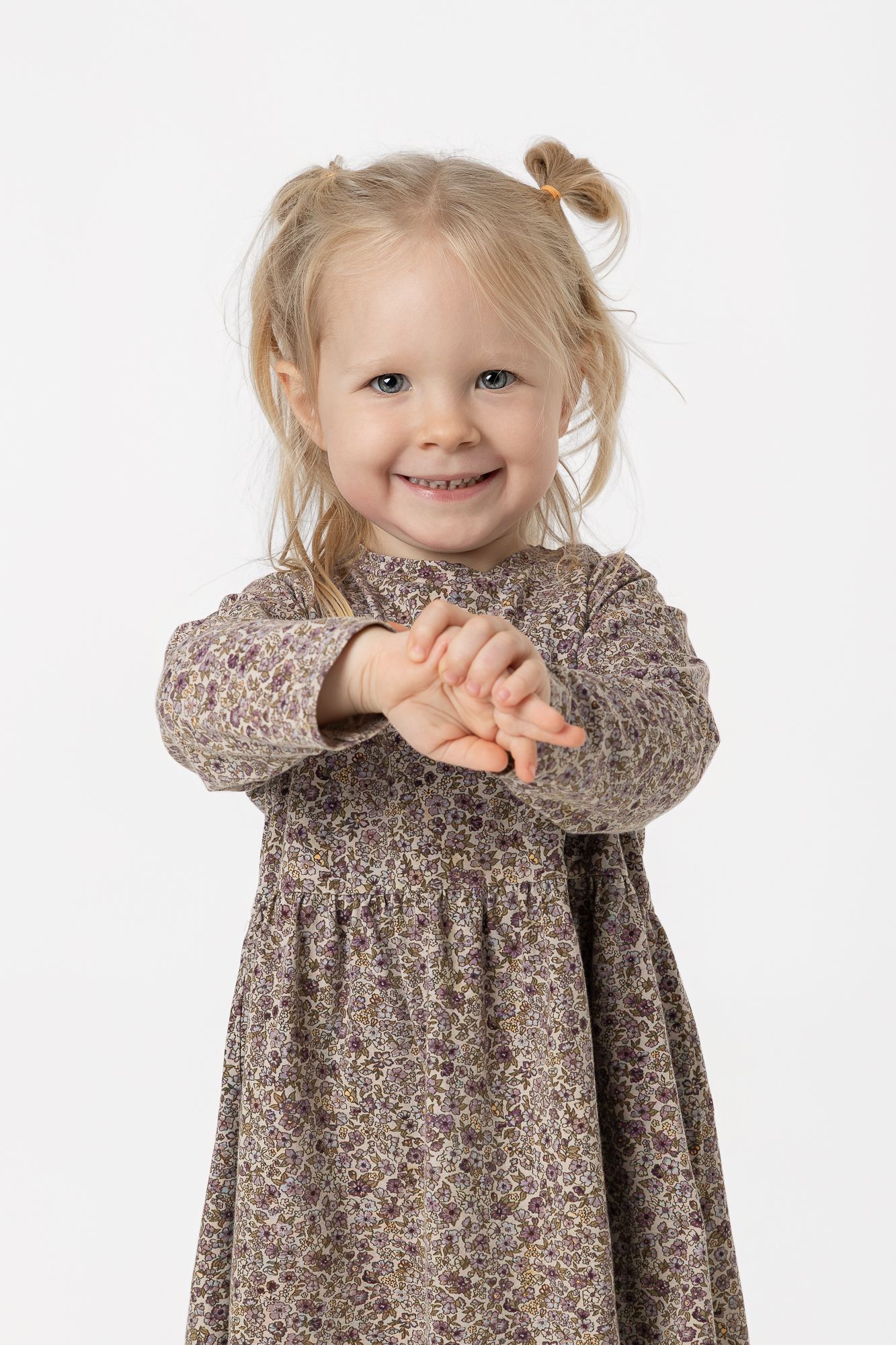 A child wearing a floral print brown dress smiles and poses against a white background in a three-photo sequence.