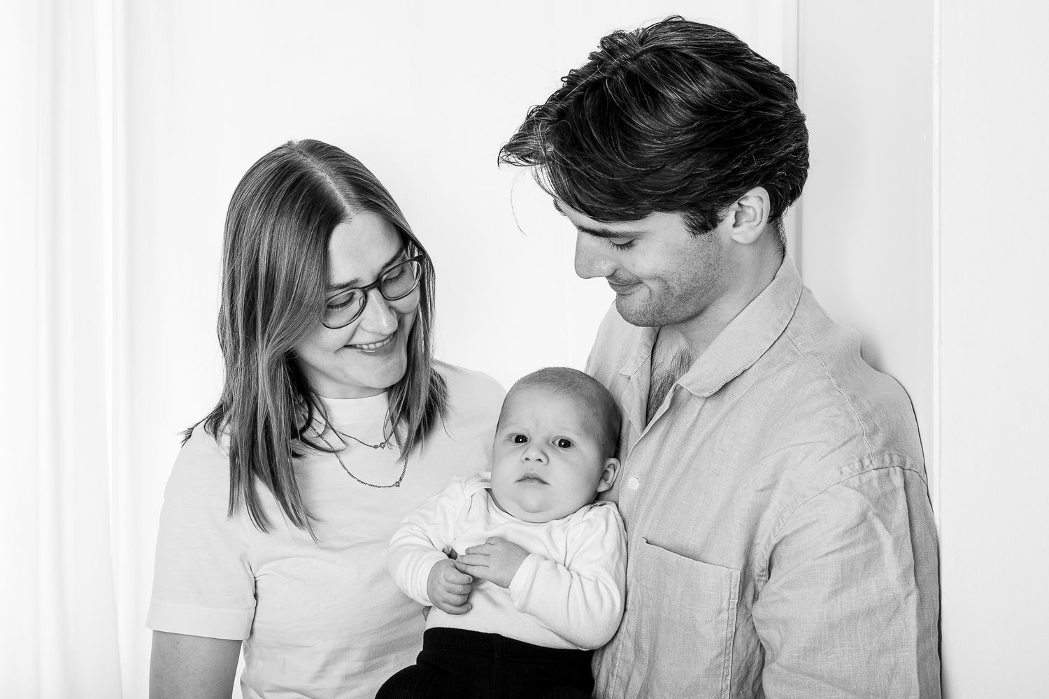 Black and white portrait of parents with a baby, mother wearing glasses and father in a button down shirt.