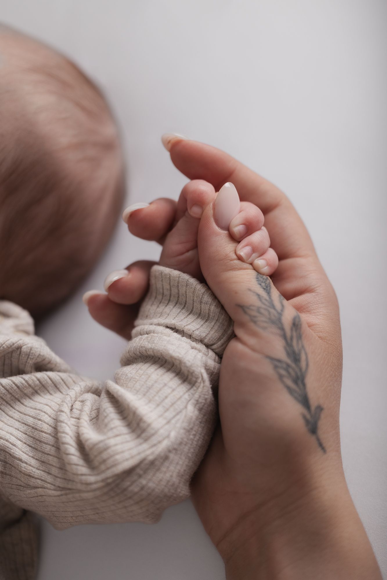 A tender moment as tiny baby fingers grasp an adult hand with a delicate feather tattoo.