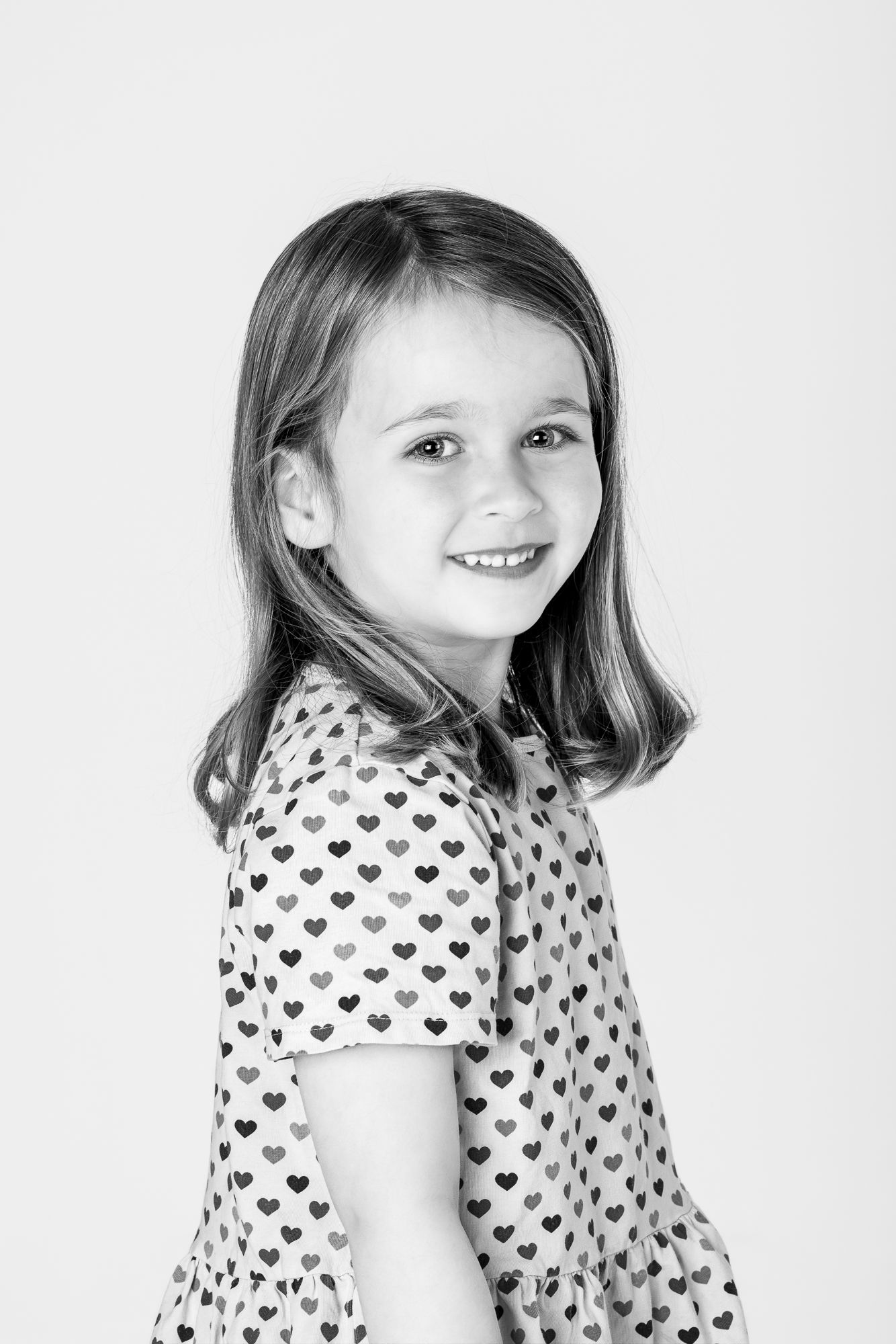 Black and white portrait series of a child wearing a heart-patterned dress against a white background.