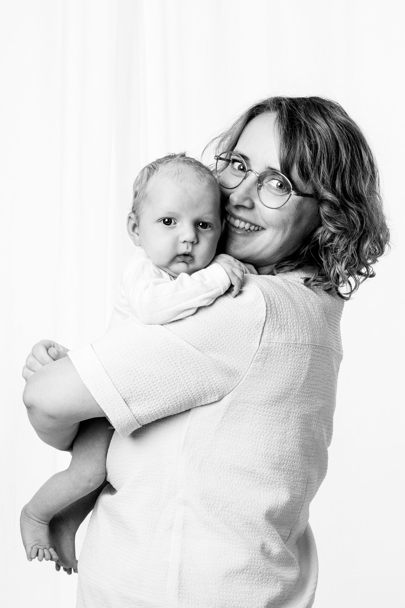 A black and white portrait of a parent  holding a baby against a white background.