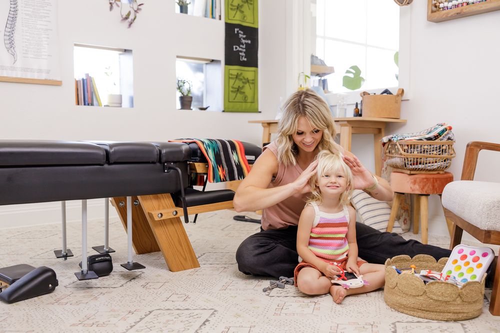 buoyant chiropractic woman practitioner in Tacoma, WA branding photo adjusting little girl while sitting on ground, girls is happy smiling