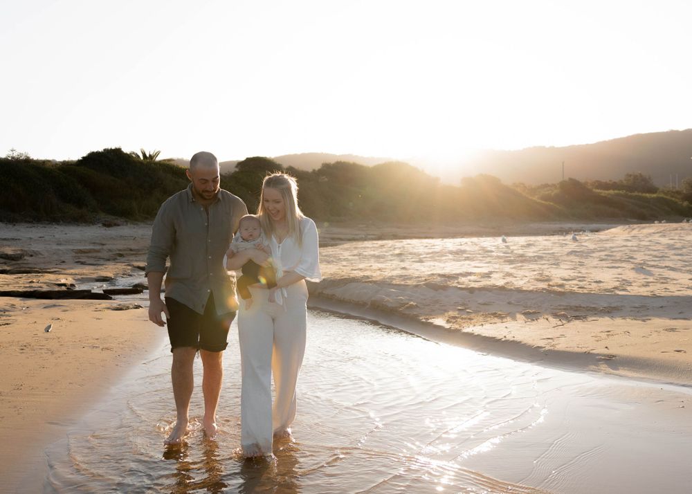 Mum, dad and their newborn baby sharing a peaceful moment on a beach in the sunshine. Family outdoor photoshoot in Wollongong and Illawarra.