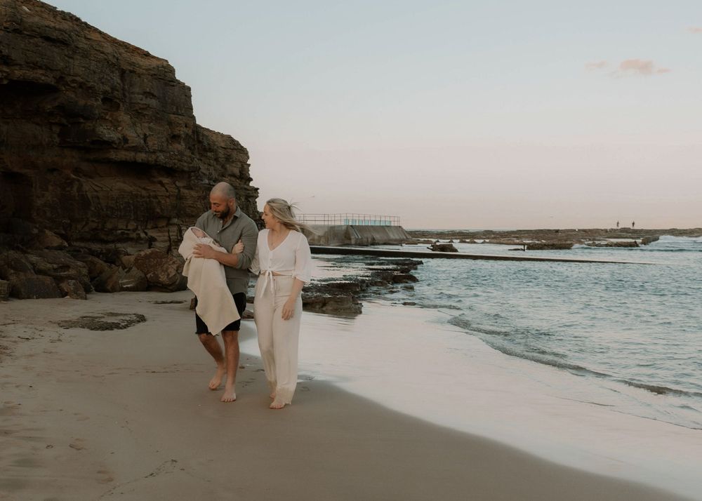 Mum, dad and their newborn baby sharing a peaceful moment on a beach in the sunset. Family outdoor photoshoot in Wollongong and Illawarra.