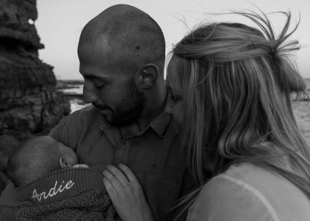 Mum, dad and their newborn baby sharing a peaceful moment on a beach in the sunshine. Family outdoor photoshoot in Wollongong and Illawarra.