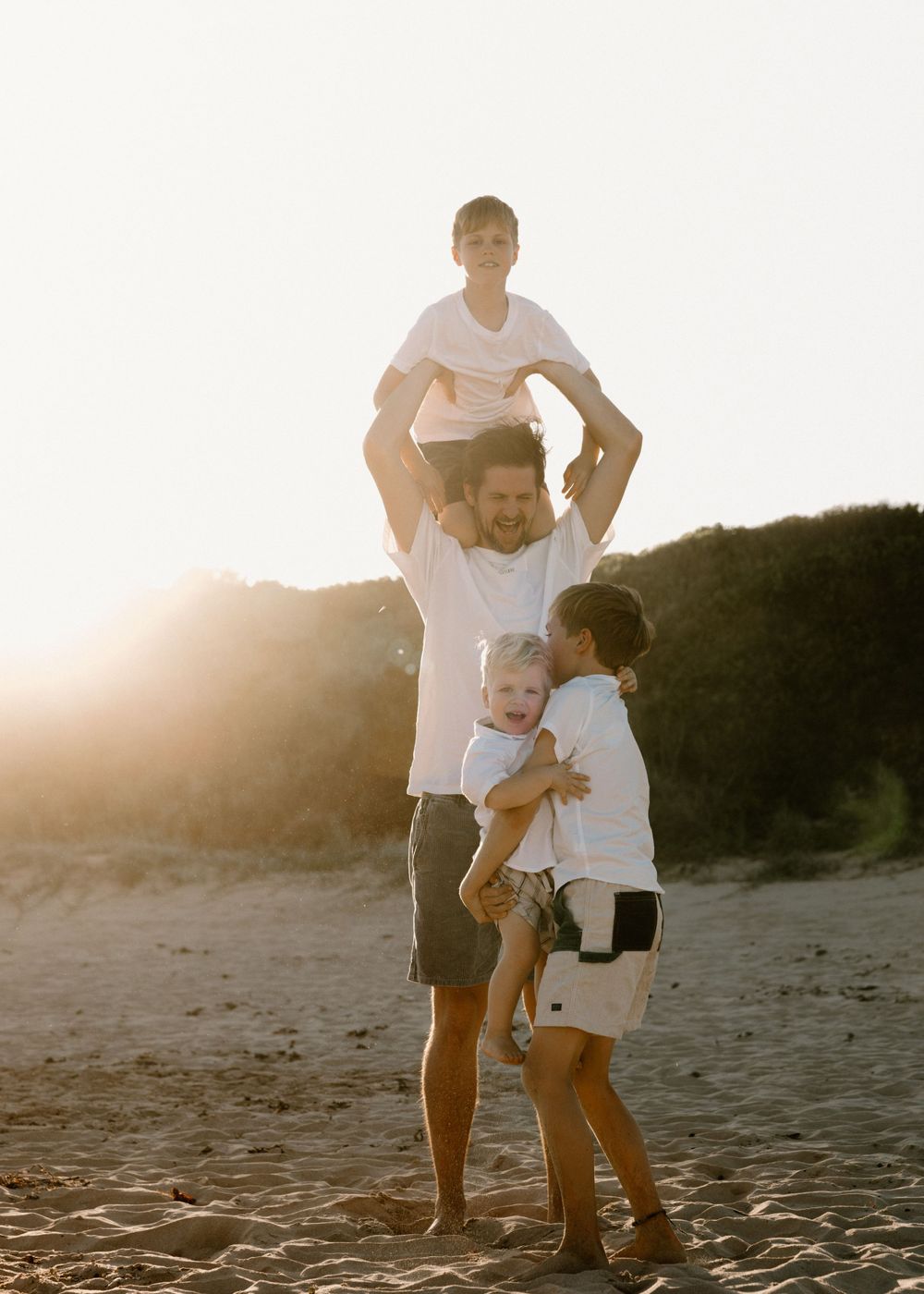 Dad and his three sons playing at Bellambi beach, dad lifting one son while the others run - family photography in Wollongong and Illawarra.