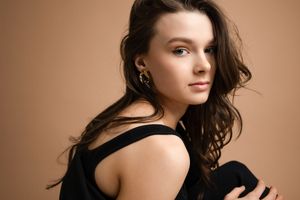 Young woman with wavy brown hair posing against a warm beige backdrop.