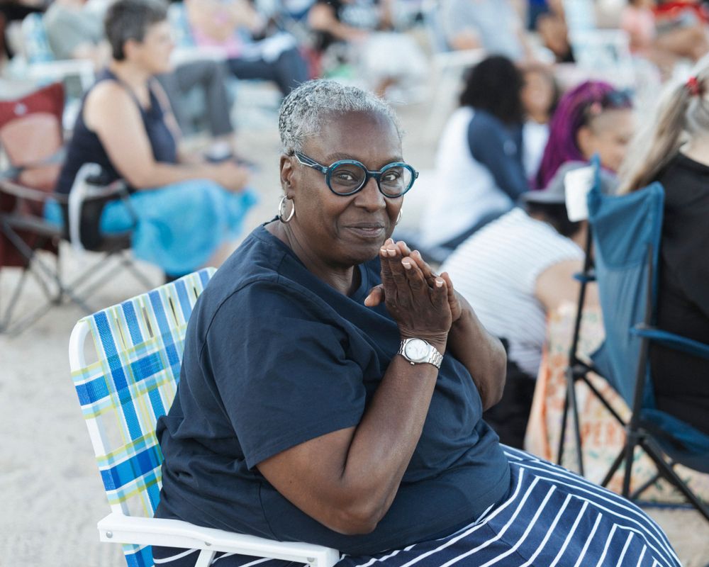 Person in navy attire sits in a folding chair at an outdoor gathering.