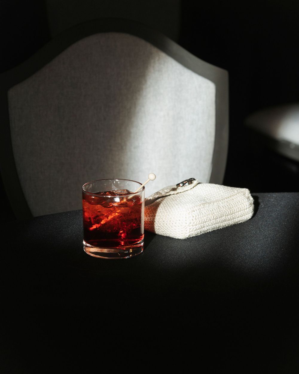 Moody still life of red cocktail and napkin on dark table with dramatic lighting.