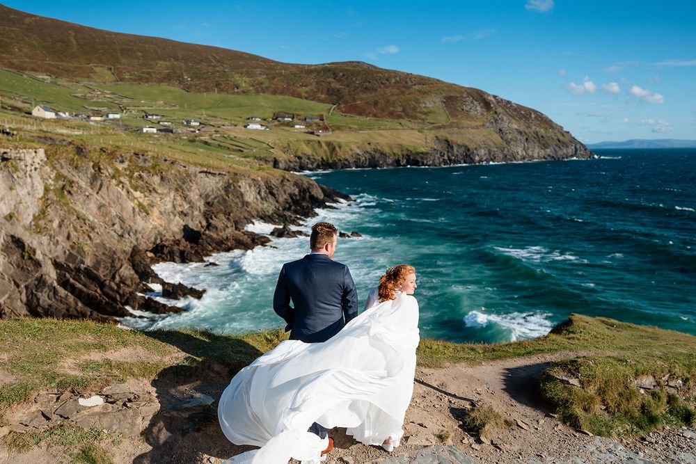 Scenic coastal view of Ireland's wild Atlantic shore with green cliffs and blue waters under bright skies.
