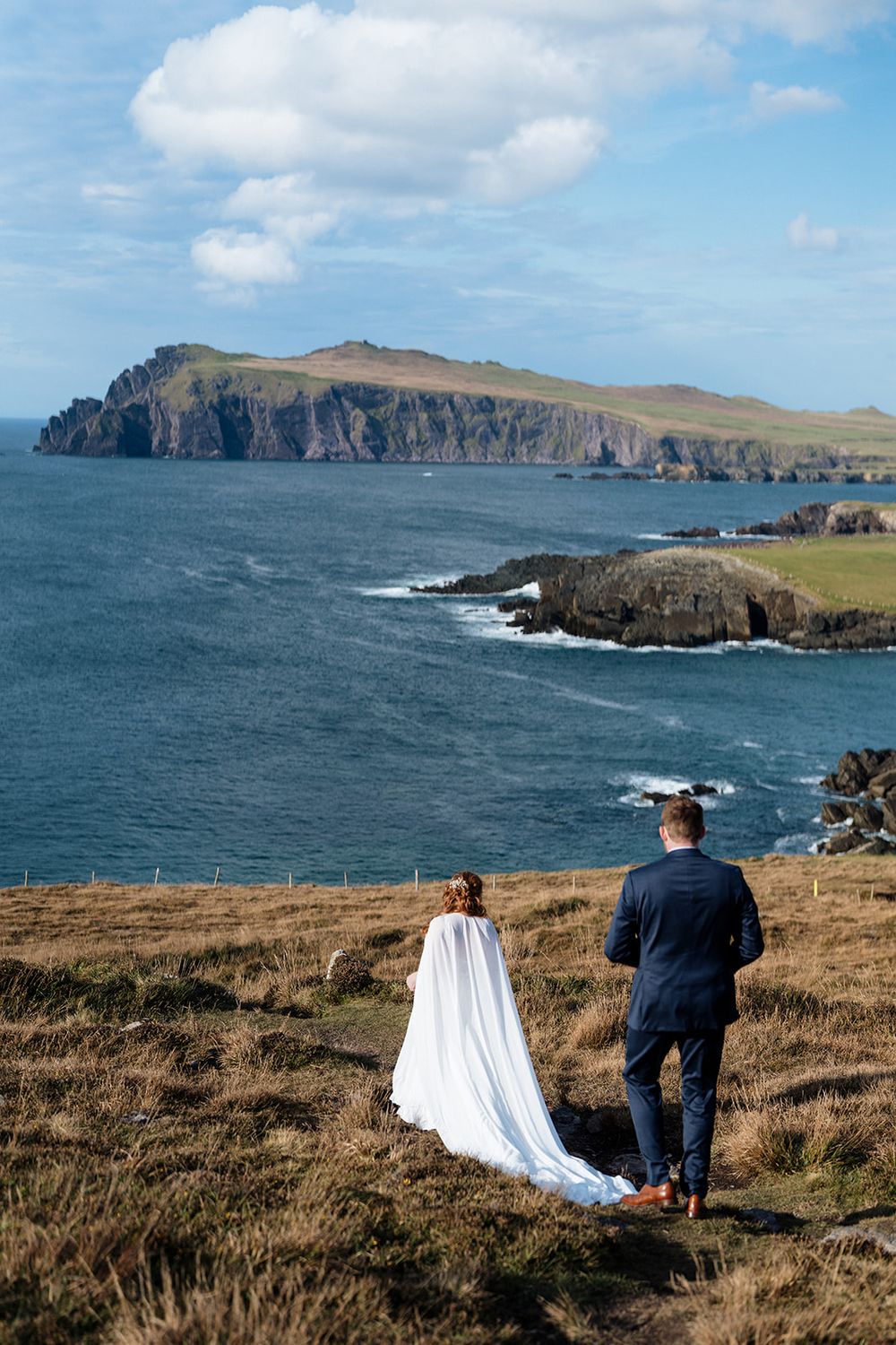 Two figures stand on a grassy cliff overlooking dramatic coastal cliffs and ocean views in Ireland.
