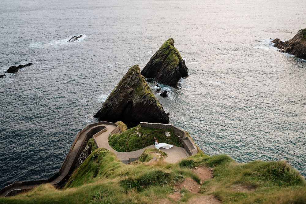 Dramatic coastal landscape featuring steep cliffs and winding paths overlooking the ocean at sunset.