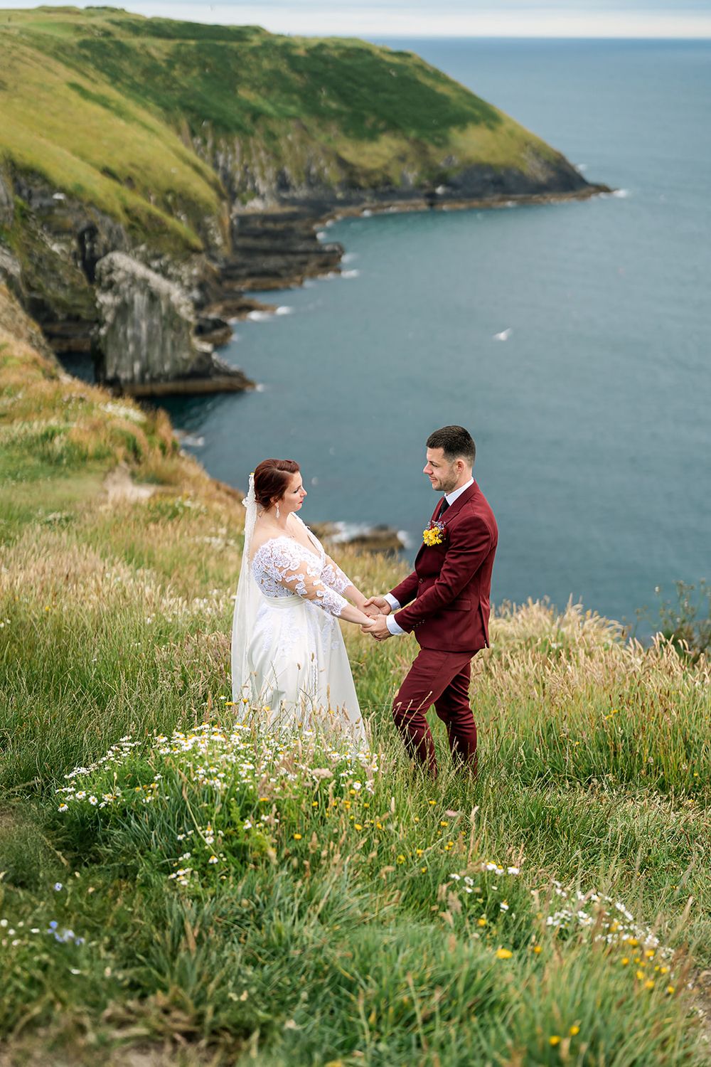 Couple shares romantic moment on grassy coastal cliffs overlooking dramatic ocean views in Ireland.