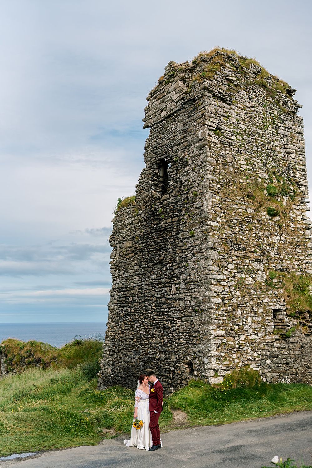 Ancient stone ruins of a medieval tower stand against cloudy skies along the Irish coastline.