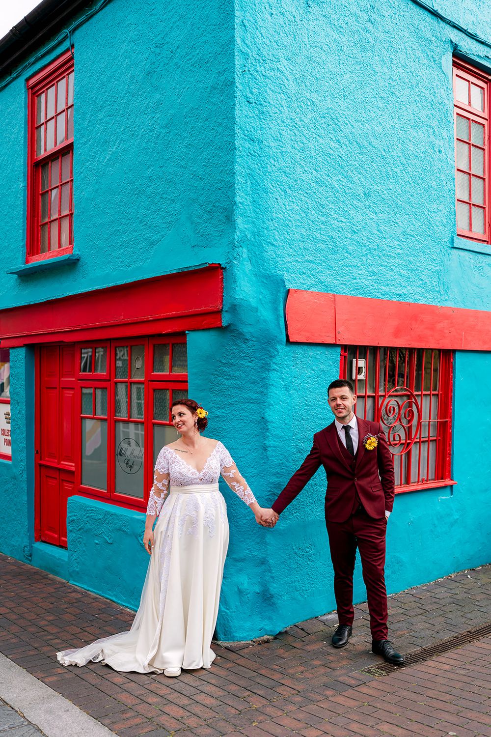 A couple in wedding attire poses against a vibrant turquoise wall with red shutters in a series of candid shots.