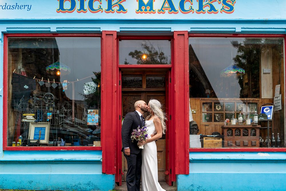 A bright blue and red storefront with large windows displays Dick Mack's signage on a traditional Irish pub building.