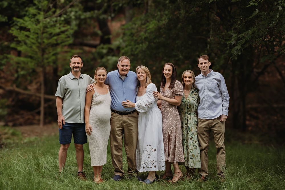 Large extended family group photo in casual attire standing together in a garden setting.