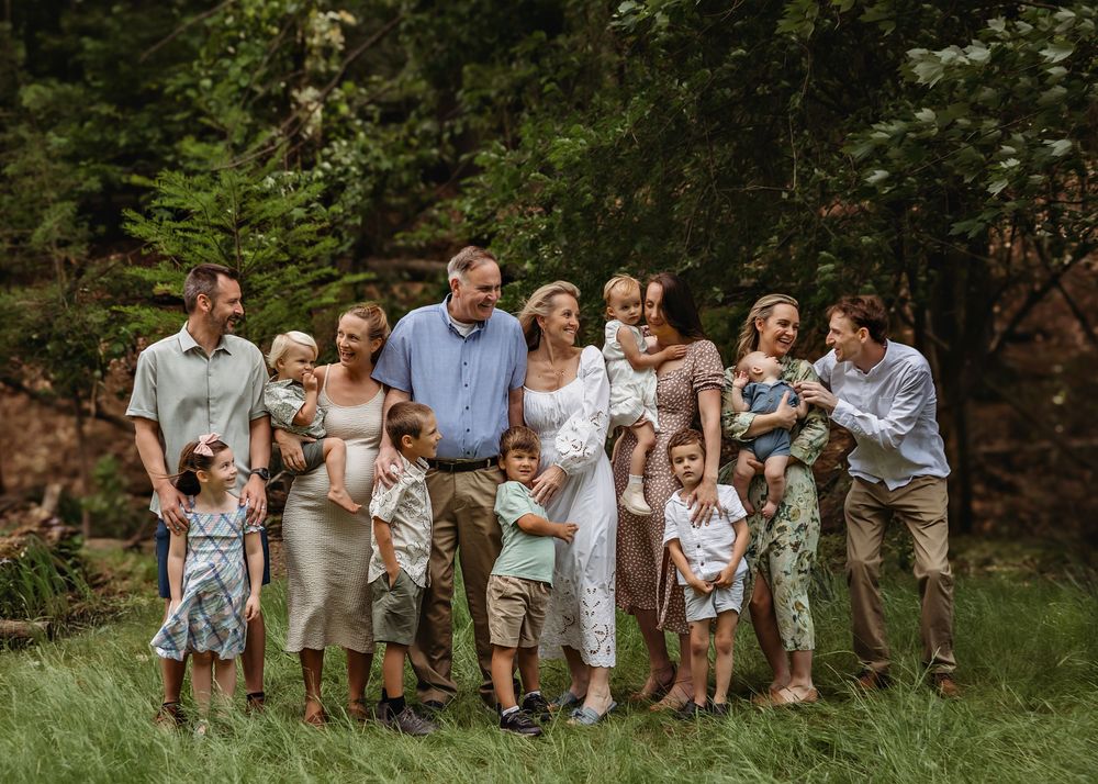Joyful extended family gathering poses informally on grassy lawn in coordinated outfits.