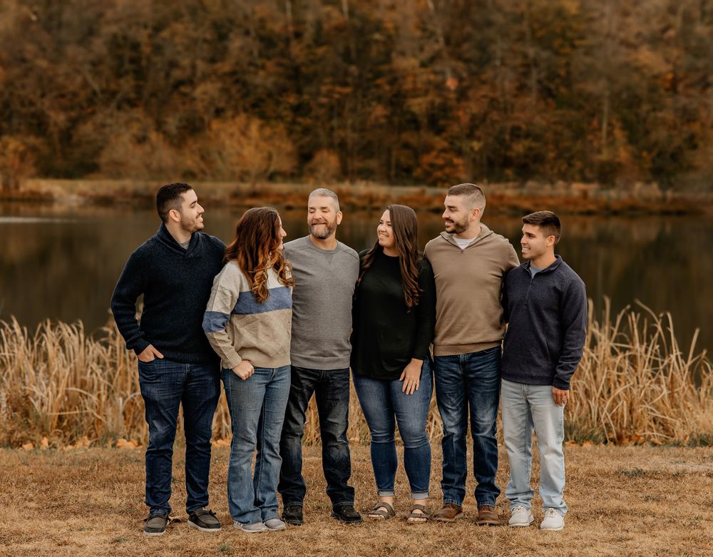 Casual family group photo with everyone wearing coordinated neutral colors by lakeside.