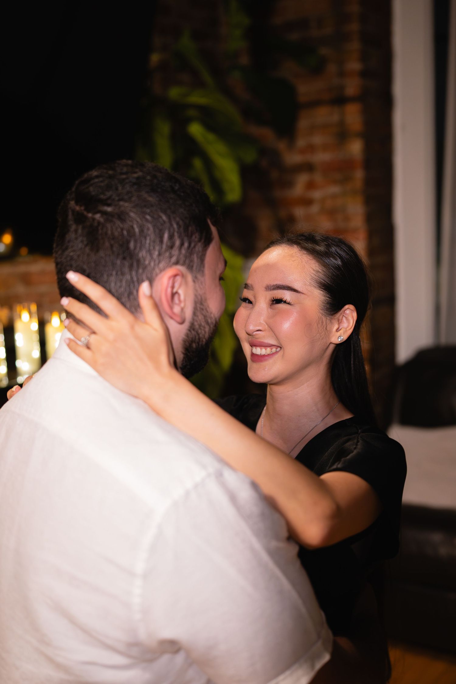 Couple dancing closely at night, smiling woman in black dress embraces man in white shirt outdoors.
