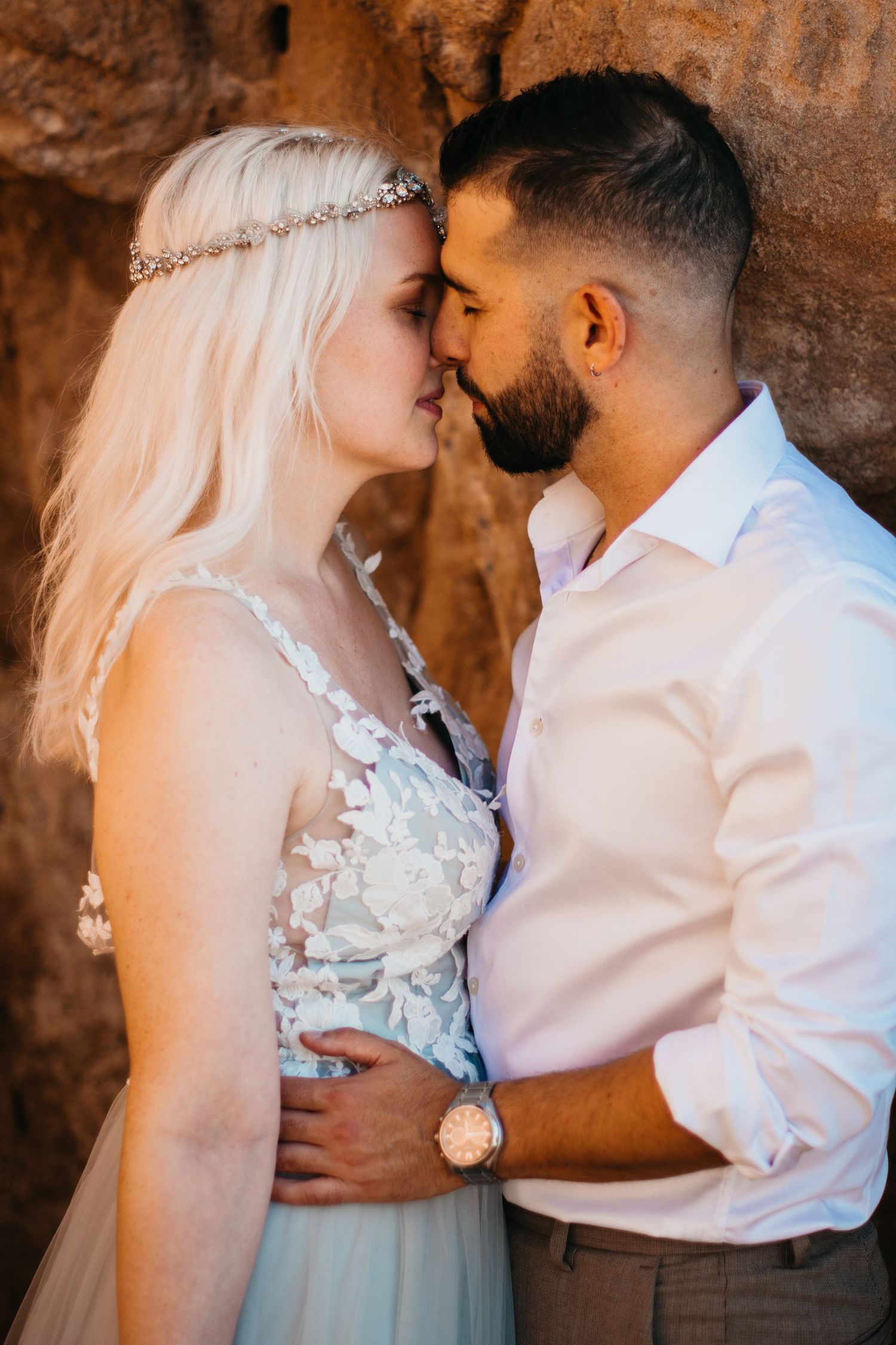 Romantic beachside wedding portrait at sunset with flowy dress and white bouquet against coastal backdrop.