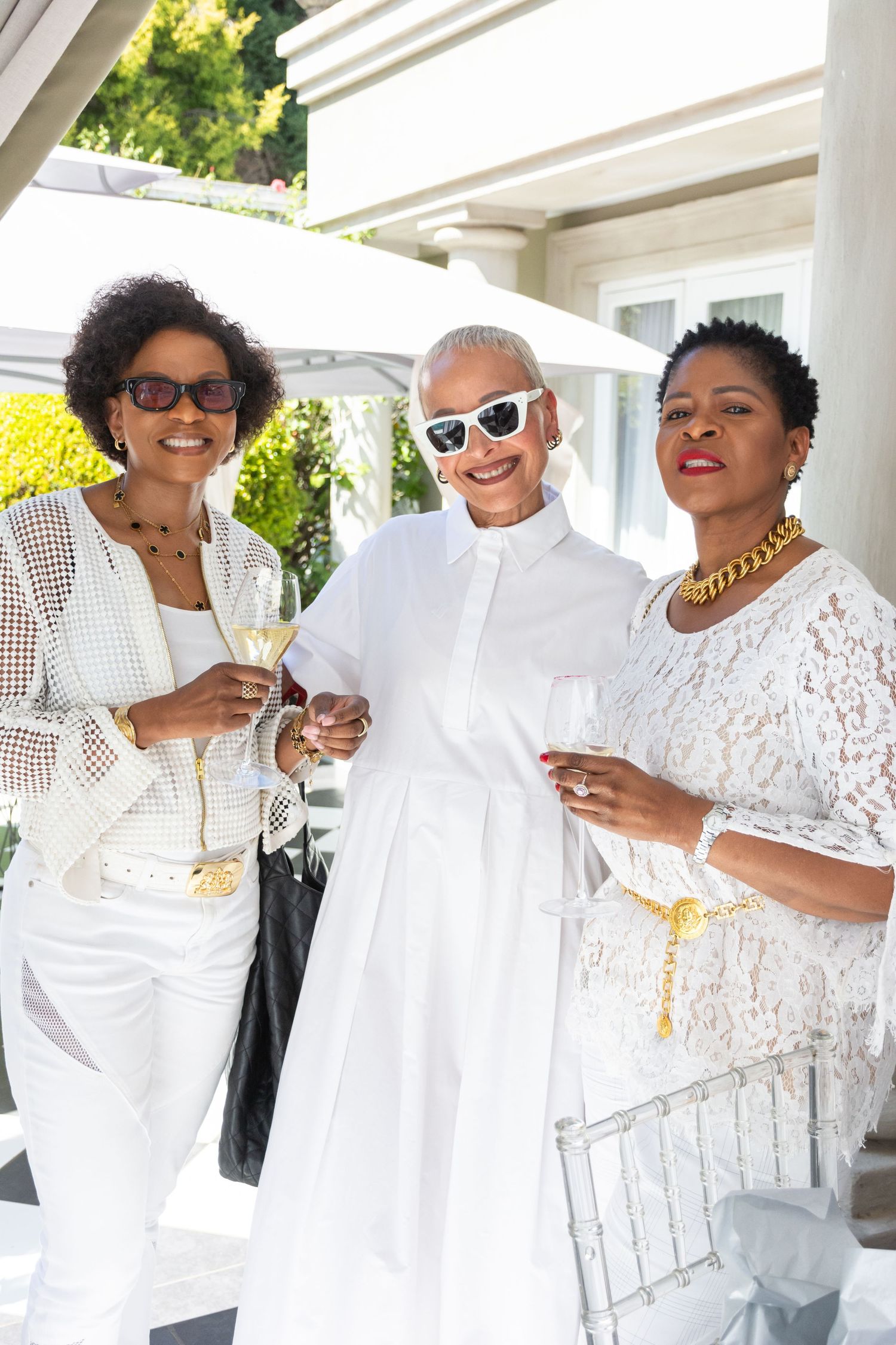 A group of women dressed in all white outfits smile and celebrate together at an outdoor event.