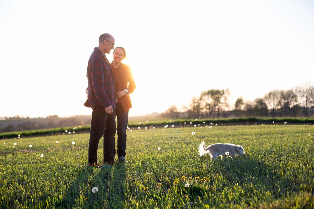 A couple embraces in a sun drenched Iowa landscape. Candid romantic engagement photography. Iowa Wedding Photographer