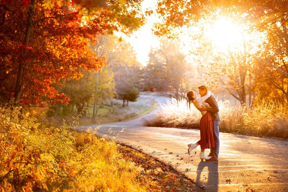 A silhouetted couple embraces in golden autumn sunlight surrounded by orange foliage.