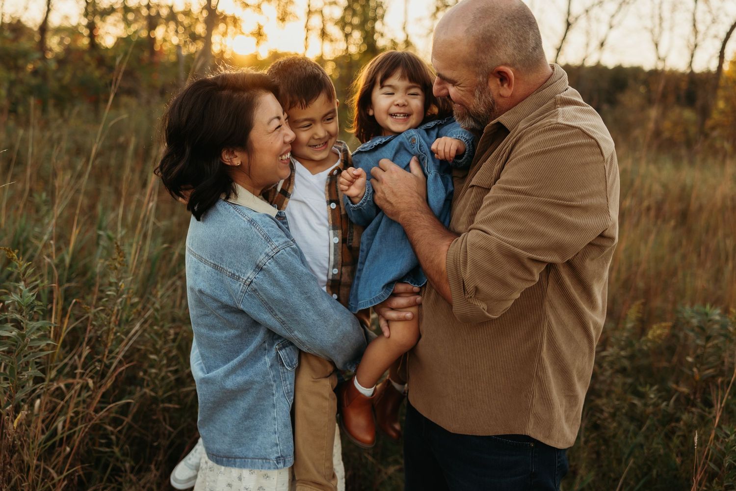 Family of four standing together in a rustic field at sunset.