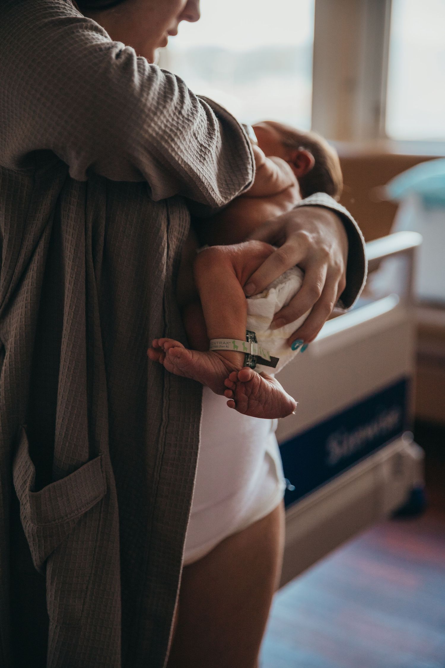 Gentle moment of parent holding newborn baby near window in soft lighting.