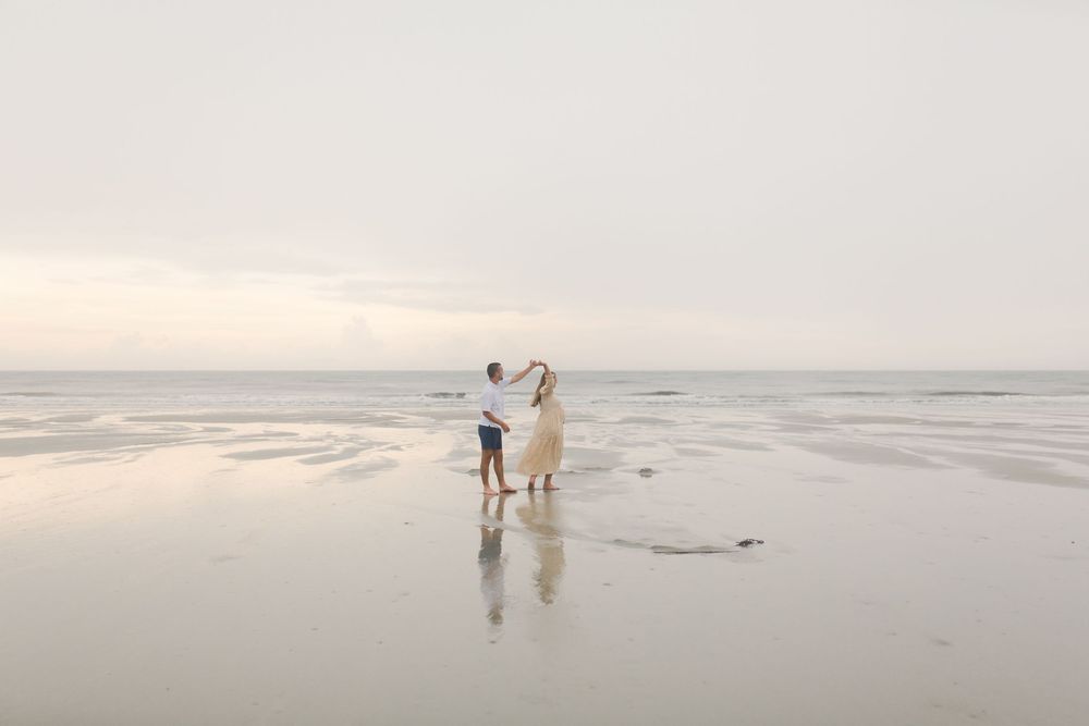 A couple dances along a misty beach at sunset creating a serene coastal scene for a Fripp Island maternity session.