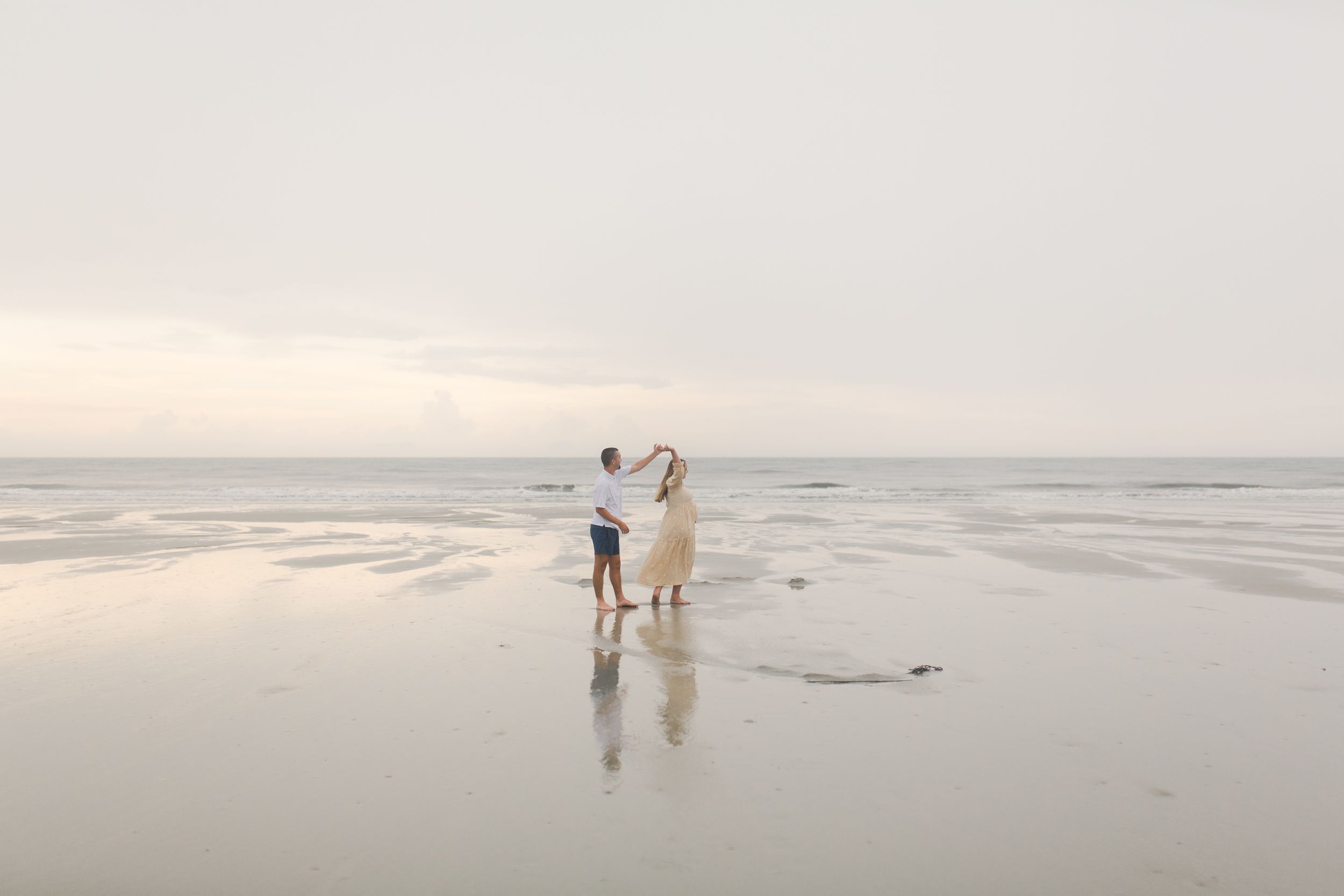 A couple dances along a misty beach at sunset creating a serene coastal scene for a Fripp Island maternity session.