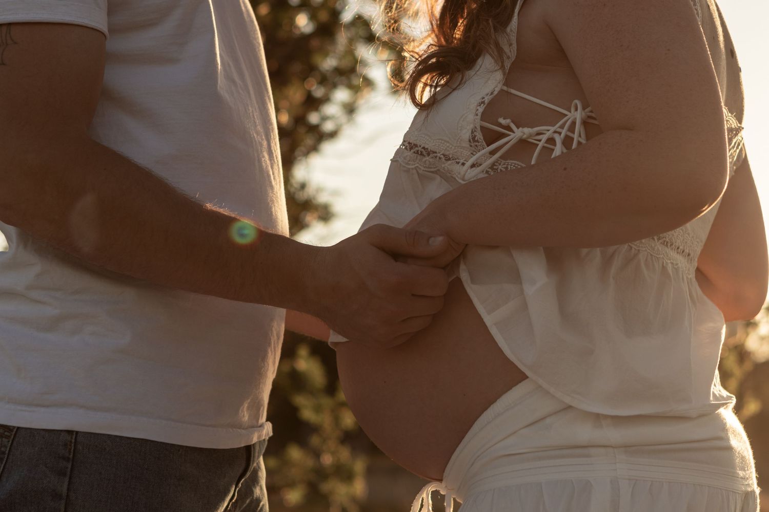 A young expecting couple wearing white looks down at mama's belly