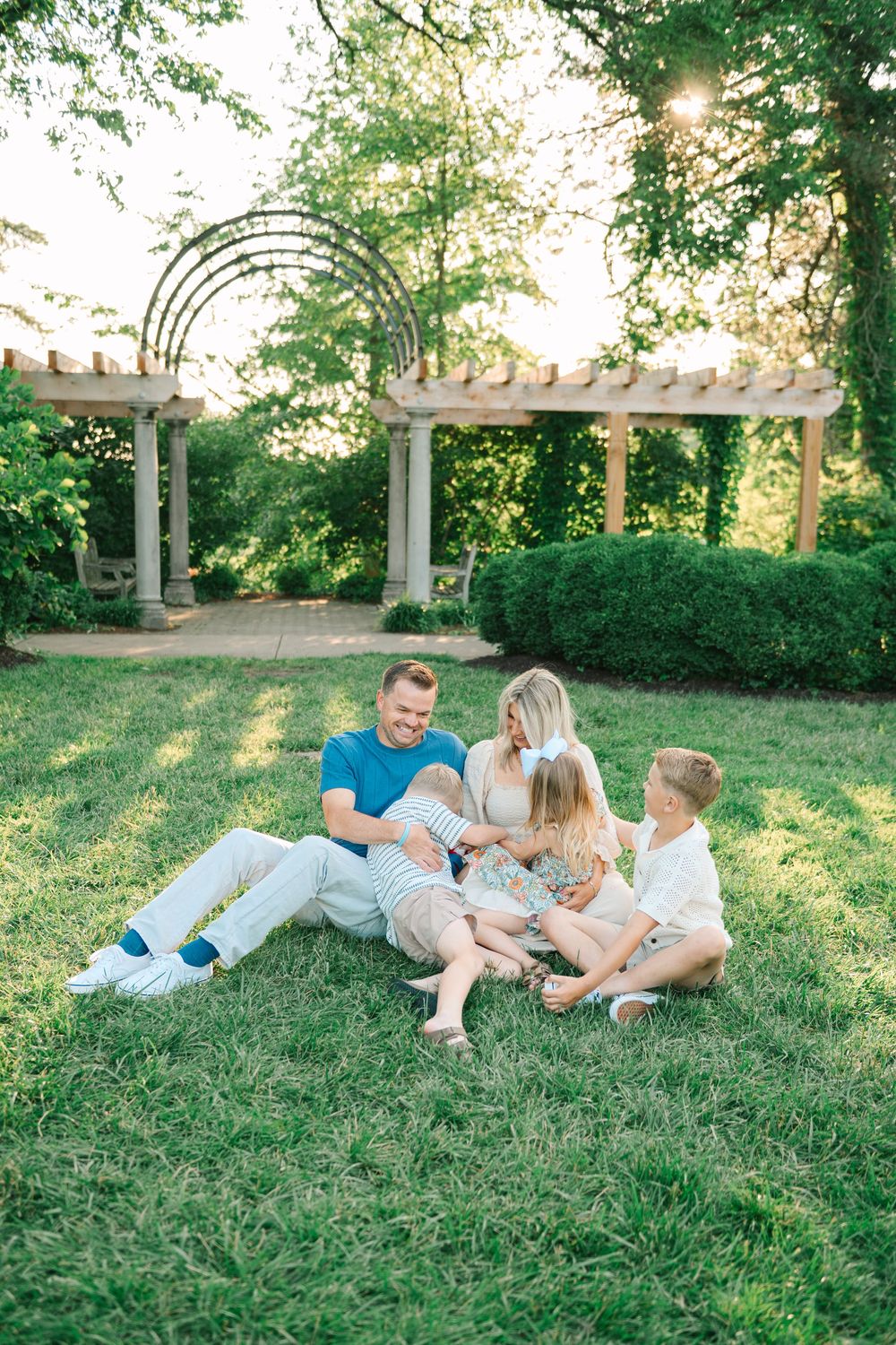Family relaxing together on a grassy hillside during a sunny summer evening.