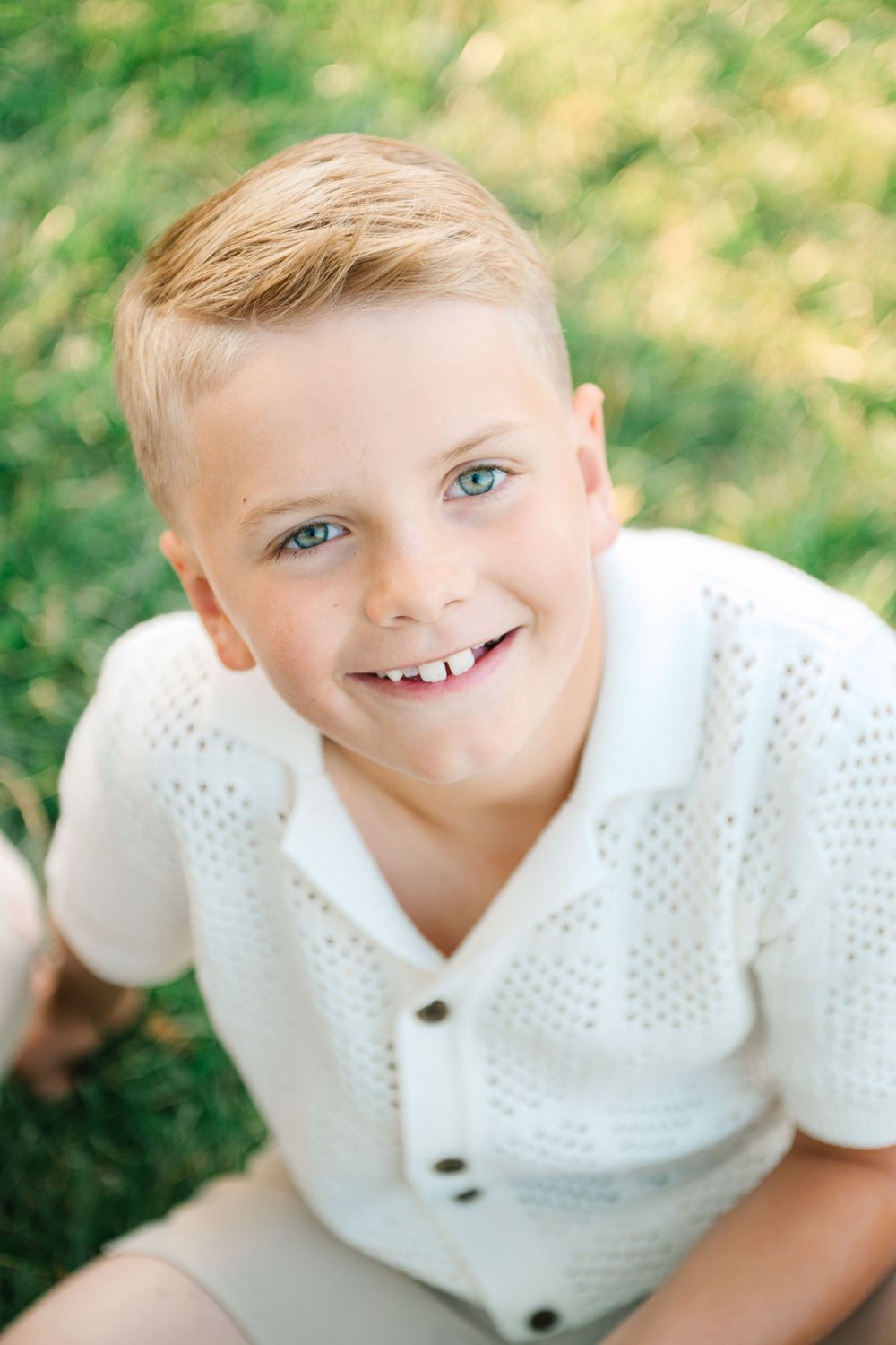 Close up portrait of smiling child wearing white polo shirt against green outdoor background.