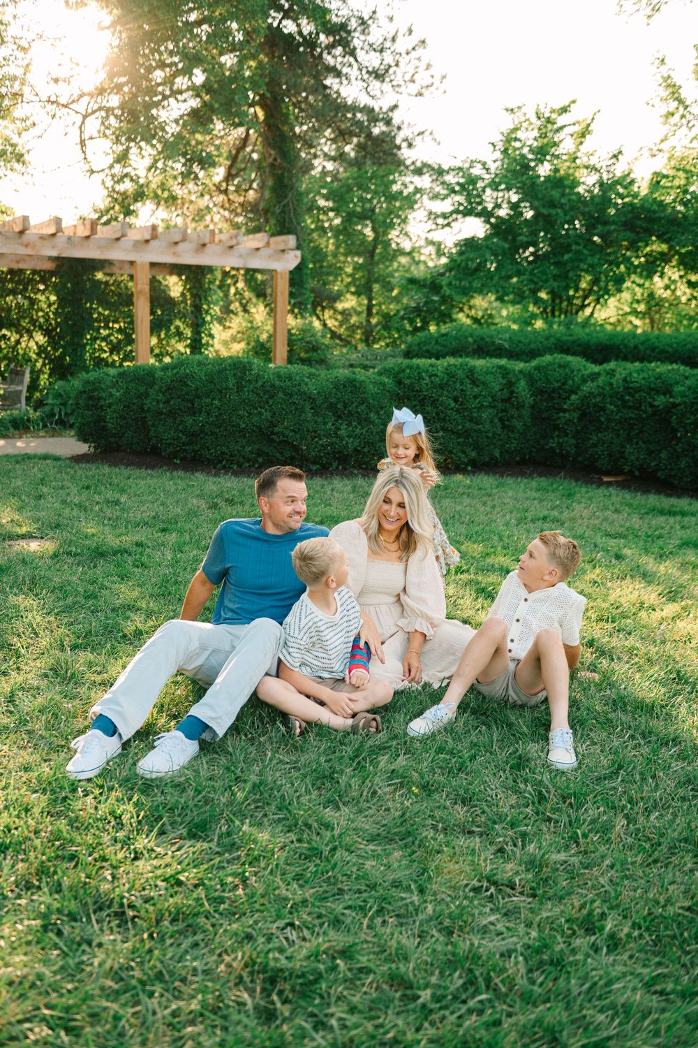 A group relaxes together on green grass during a sunny afternoon in a garden setting.