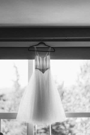 A white wedding dress hangs elegantly on a hanger against a bright window.