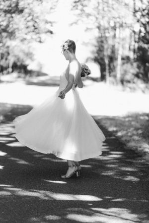 A person in a white dress twirls on a tree-lined path creating elegant movement.