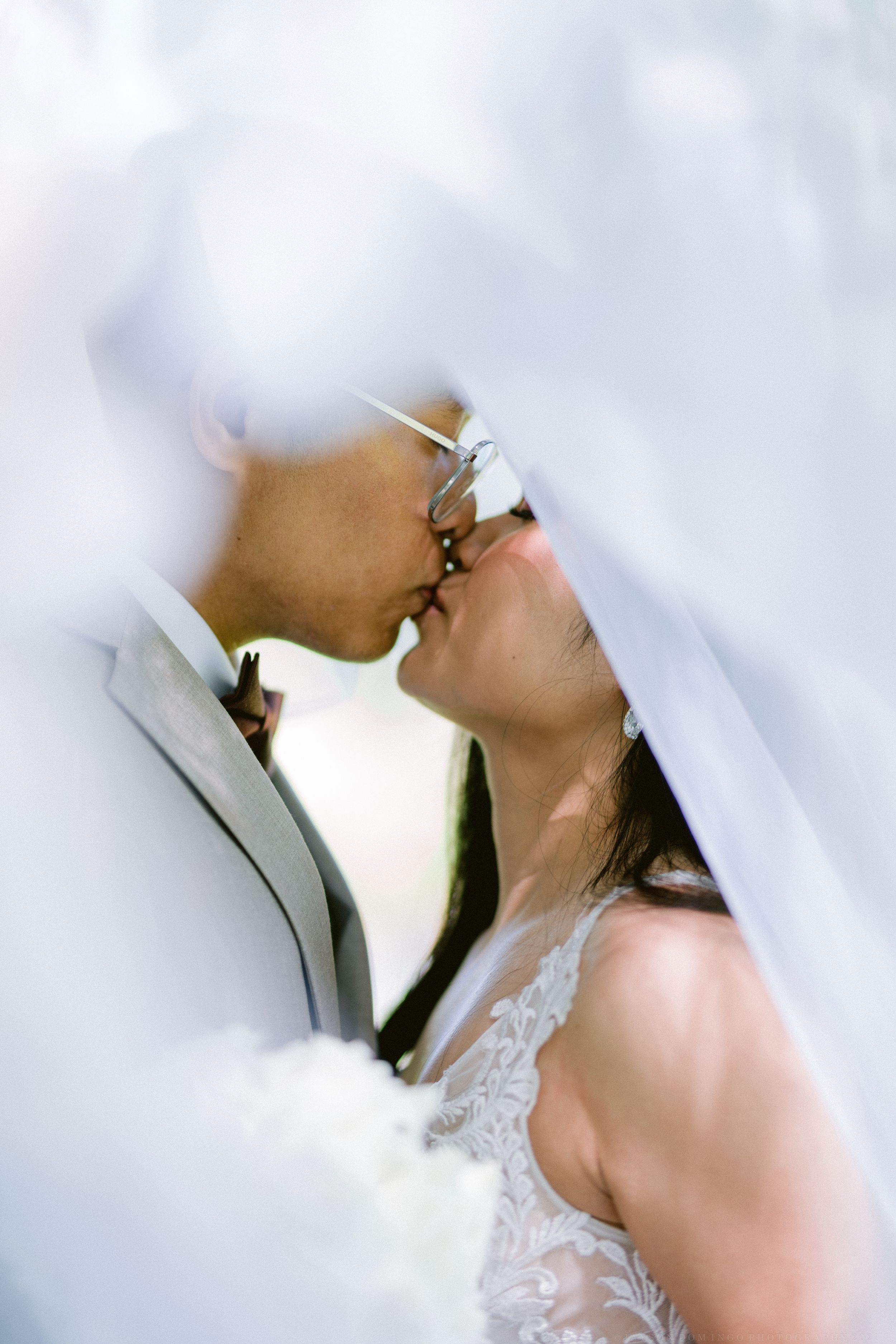 Bride and groom sharing a romantic kiss under a flowing white veil on their wedding day.